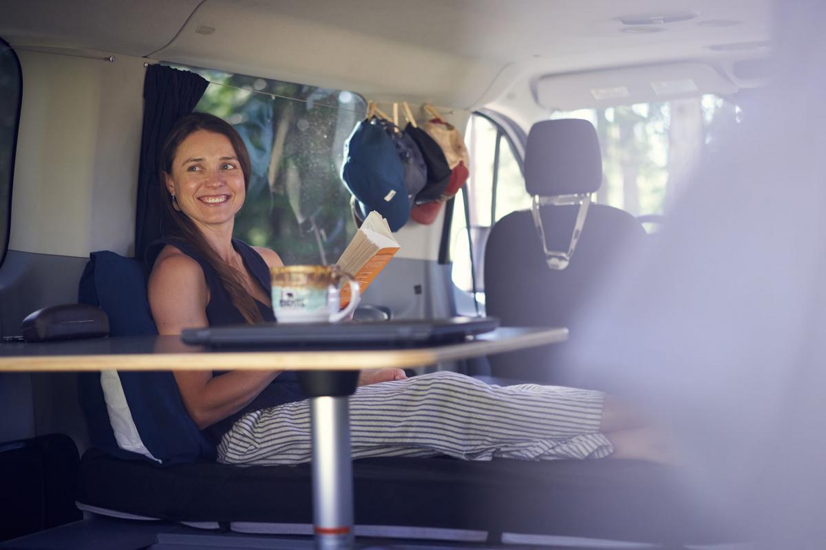 a woman sitting in a van with a cup of coffee.