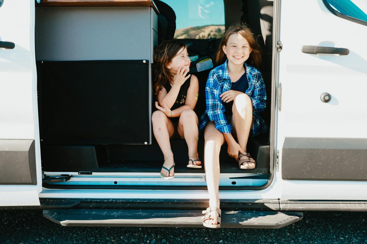 two girls sitting in the door of a van.